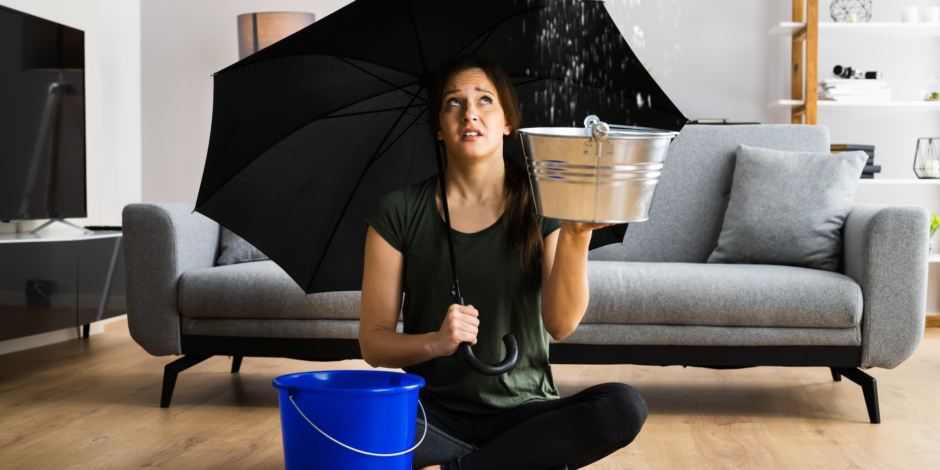 Dégâts des eaux plafond : une femme avec un parapluie et un seau tente de contenir une fuite d’eau dans son salon.