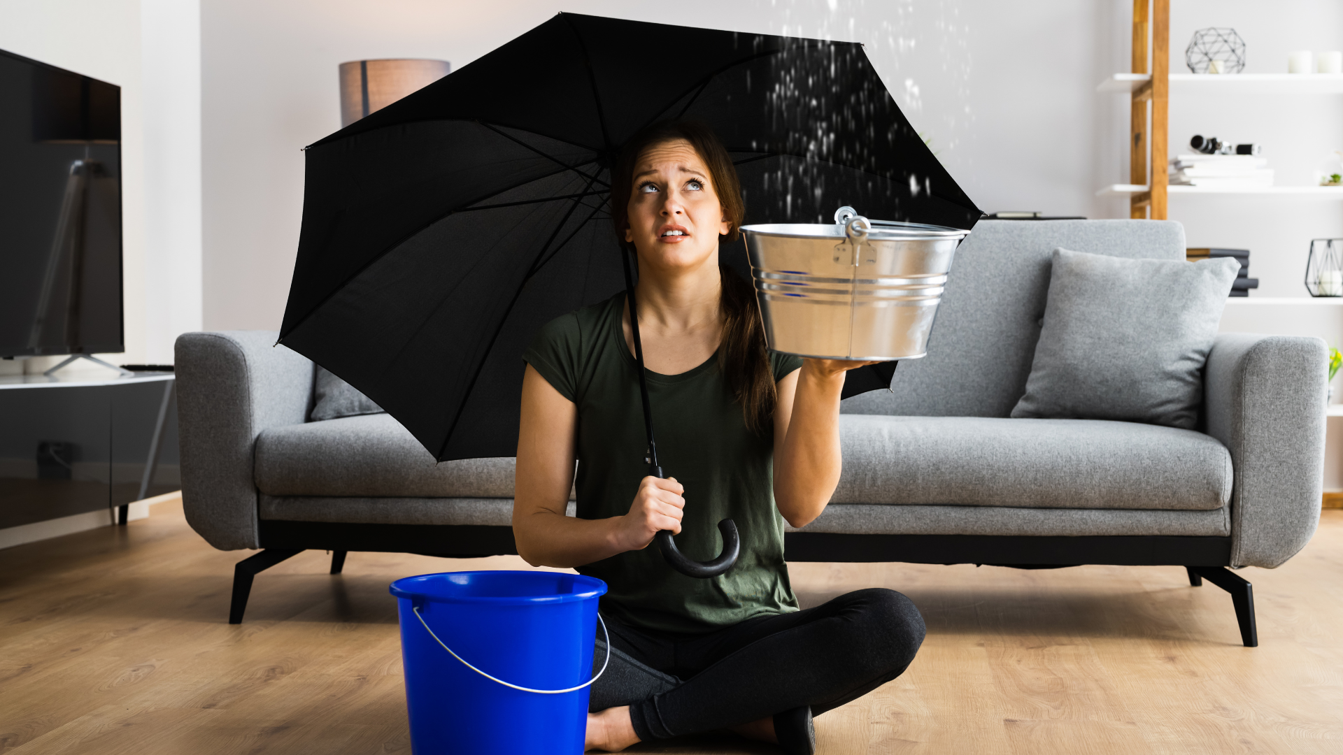 Dégâts des eaux plafond : une femme avec un parapluie et un seau tente de contenir une fuite d’eau dans son salon.