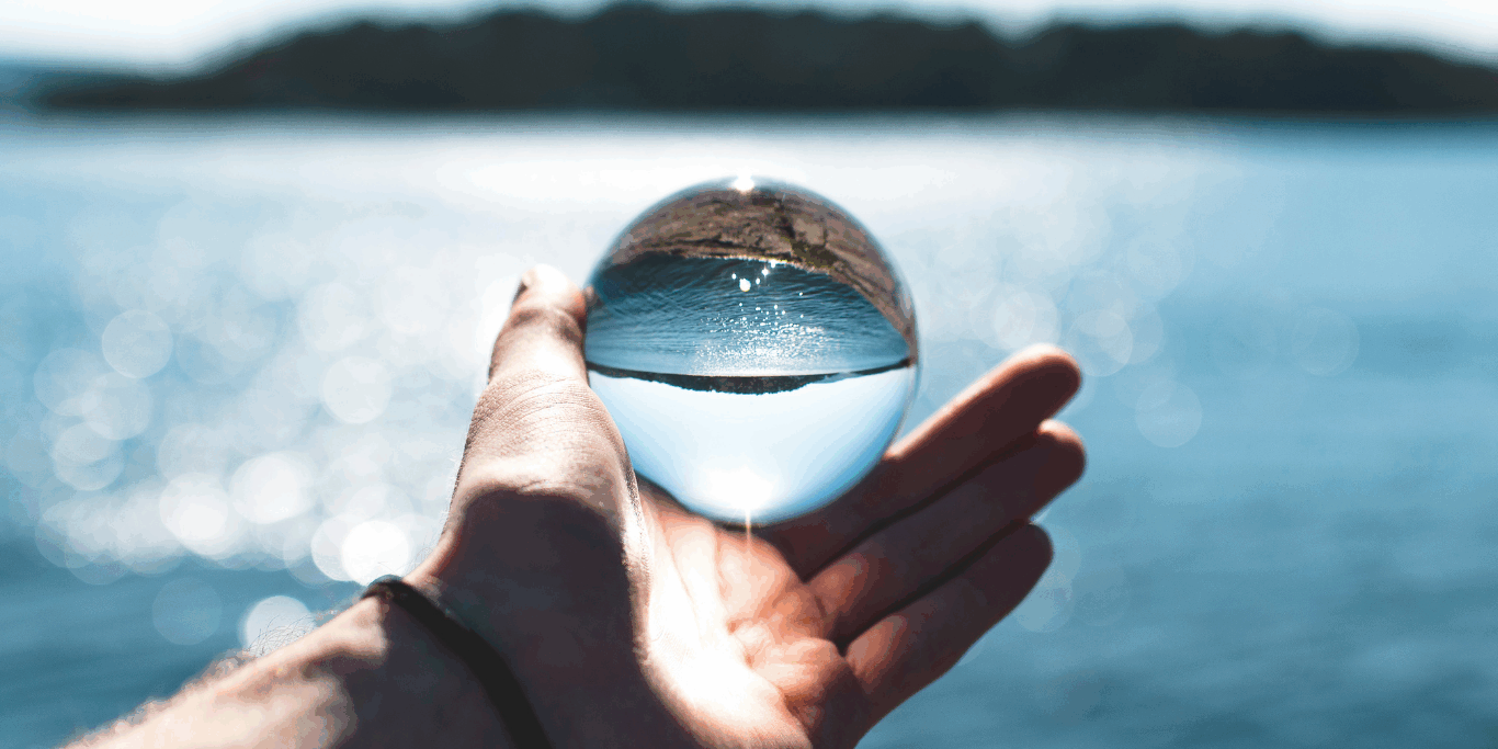 Main tenant une sphère translucide reflétant un paysage avec de l’eau, symbolisant les enjeux de restrictions d’eau et la fragilité des ressources hydriques.