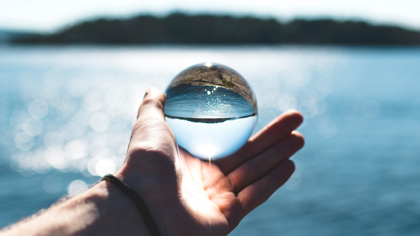 Main tenant une sphère translucide reflétant un paysage avec de l’eau, symbolisant les enjeux de restrictions d’eau et la fragilité des ressources hydriques.